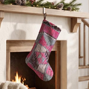 Könnte beinhalten: Ein Weihnachtsstrumpf mit einem gewebten, mehrfarbigen geometrischen Muster in leuchtendem Pink, Schieferblau und dunklem Anthrazitgrau. Der Strumpf besteht aus strukturiertem Stoff und hat eine Schlaufe an der Oberseite zum Aufhängen an einem Haken.