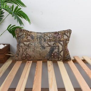 May include: A rectangular throw pillow with a vintage floral pattern in shades of brown, pink, and blue. The pillow is lying on a wooden slatted bed frame.