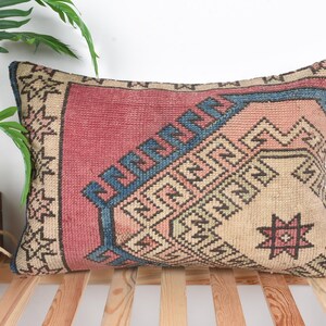 Könnte beinhalten: Rechteckiges Zierkissen mit einem geometrischen Muster in Rot-, Beige- und Blautönen. Das Kissen hat ein zentrales Design mit einem Stern und einen Rand mit einem sich wiederholenden Muster. Das Kissen liegt auf einer Holzoberfläche.