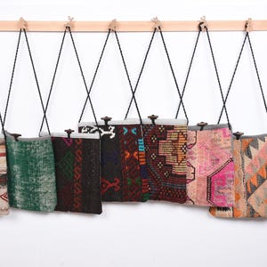 May include: Eight colorful patterned fabric bags hanging on a wooden rack. The bags are made from recycled rugs and have a variety of colors and designs.