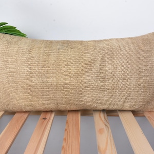 May include: A light brown rectangular pillow with a woven texture. The pillow is sitting on a wooden slatted surface.