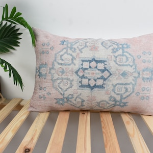 May include: A pink and blue patterned throw pillow with a geometric design. The pillow is on a wooden slatted surface.