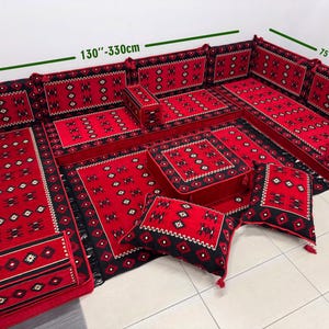 Puede incluir: Un juego de asientos de suelo rojo y negro con un patrón geométrico. El conjunto incluye varias piezas, como asientos de esquina, cojines y una otomana rectangular. Las dimensiones son de 330 cm a 838 cm, 190 cm a 483 cm y 71 cm a 178 cm.