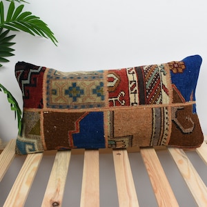 May include: A rectangular cushion with a patchwork design featuring various shades of brown, blue, red, and beige. The cushion is made of woven fabric with intricate patterns and is resting on a wooden slatted surface.