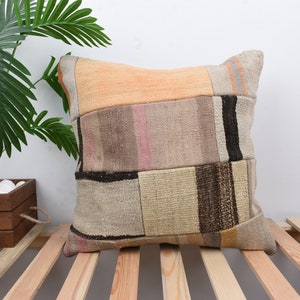 Könnte beinhalten: Ein Patchwork-Wurfkissen in beige, braun und orange. Das Kissen ist aus gewebtem Stoff und hat eine rechteckige Form.