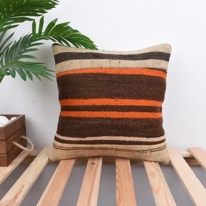May include: A brown and orange striped throw pillow with a beige background. The pillow is made of woven fabric and has a fringed edge.