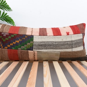May include: A long, rectangular pillow with a patchwork design. The pillow is made of different fabrics in shades of red, brown, beige, and white. The pillow is sitting on a wooden slatted surface.