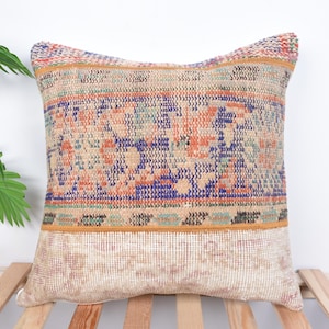 May include: A square throw pillow with a beige background and a colorful geometric pattern. The pattern features shades of blue, orange, green, and yellow. The pillow has a fringe border.