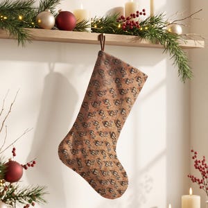 Könnte beinhalten: Ein Weihnachtsstrumpf aus strukturiertem Stoff in warmen Farbtönen mit einem sich wiederholenden dunkelblauen und schwarzen geometrischen Muster. Der Strumpf hat oben eine einfache braune Aufhängeschlaufe und hängt vor einer hellen Wand.