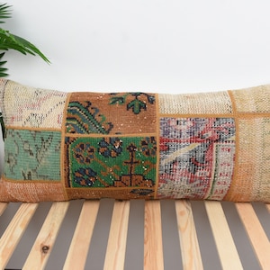May include: A long rectangular pillow with a patchwork design. The pillow is made of different pieces of fabric in shades of brown, green, beige, and red. The fabric has a woven texture and features intricate patterns.