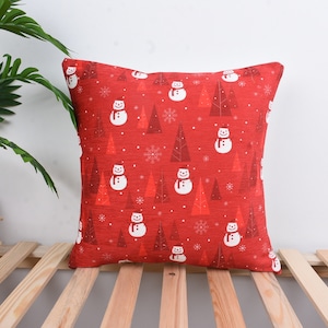 May include: Red throw pillow with a white snowman and pine tree pattern.