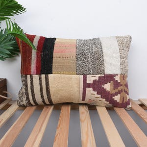 Puede incluir: Una almohada rectangular con un diseño de patchwork en varios tonos de marrón, rojo, blanco y negro. La almohada está hecha de tejido tejido y tiene un aspecto ligeramente desgastado.