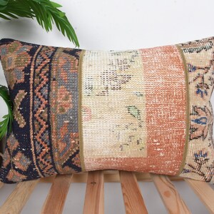 Puede incluir: Cojín decorativo rectangular con diseño patchwork. El cojín presenta secciones en azul marino, beige y coral con patrones intrincados. El cojín está colocado sobre una superficie de listones de madera.