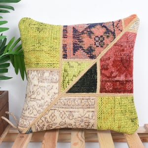 Peut inclure: Coussin carré en patchwork avec une variété de couleurs et de textures. Le coussin présente un motif géométrique avec des sections de tissus verts, rouges, noirs et beiges. Le coussin est posé sur une surface en bois.