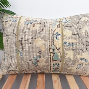 May include: Rectangular decorative pillow with a vintage rug design. The pillow features a beige and gray color scheme with blue and cream floral patterns. Two vertical beige stripes run down the center of the pillow.