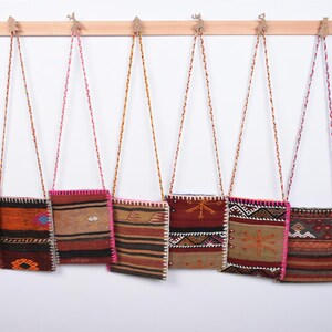 May include: Eight colorful woven tapestry bags hanging on hooks. The bags have different patterns and colors, including red, orange, brown, and white.