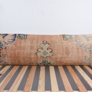 Può includere: Un cuscino lungo e rettangolare con sfondo beige e un motivo floreale colorato. Il cuscino è realizzato in tessuto tessuto e ha un bordo con frange.