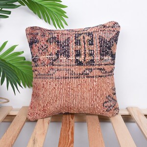 May include: A square cushion with a woven fabric cover. The cushion has a brown and blue geometric pattern. The cushion is sitting on a wooden slatted surface.