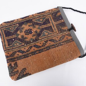 May include: A small, brown and blue patterned bag with a black strap and a wooden toggle closure. The bag is made from a woven fabric with a traditional design.
