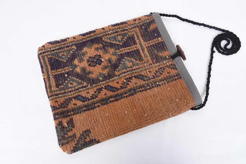 May include: A small, brown and blue patterned bag with a black strap and a wooden toggle closure. The bag is made from a woven fabric with a traditional design.