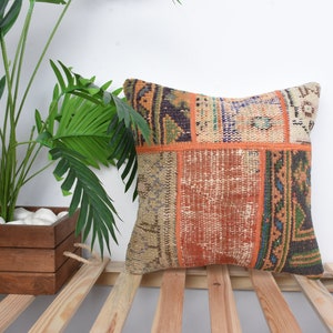 May include: A colorful patchwork pillow cover with a mix of orange, brown, beige, green, and blue tones. The pillow cover is made from recycled materials and has a unique, handmade look.