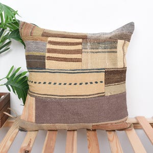 May include: A brown, beige, and gray patterned throw pillow with a woven texture. The pillow is sitting on a wooden slatted surface.