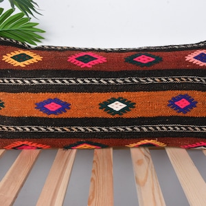 Puede incluir: Un cojín lumbar marrón, negro, naranja, rosa, azul y blanco con un diseño tejido.