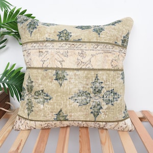 May include: A decorative throw pillow with a beige background and a pattern of green leaves. The pillow has a fringed edge and is made of a soft, woven fabric.