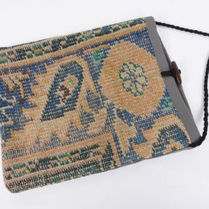 May include: A small, rectangular bag with a patterned fabric front and a gray canvas back. The bag has a black strap and a wooden toggle closure.
