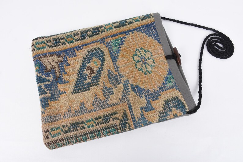 May include: A small, rectangular bag with a patterned fabric front and a gray canvas back. The bag has a black strap and a wooden toggle closure.