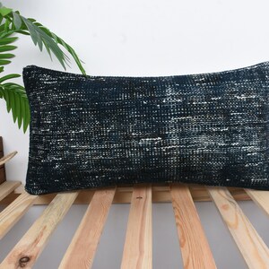 May include: A dark blue and white patterned cushion with a rectangular shape. The cushion is made of a soft, woven fabric and is resting on a wooden slatted surface.