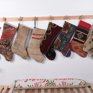 May include: Nine colorful Christmas stockings made from vintage rugs are hanging on a wooden rod. The stockings are decorated with various patterns and colors, including red, green, blue, and brown.