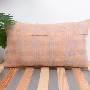 May include: A soft, peach-colored pillow with a subtle checkered pattern. The pillow is made of a woven fabric and has a simple, rustic look.