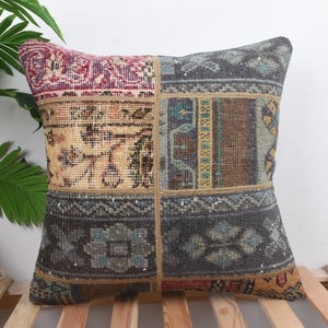 May include: Square decorative pillow with a patchwork design. The pillow features a mix of colors including burgundy, beige, teal, and gray. The pillow is made of a textured fabric and has a vintage or antique aesthetic.