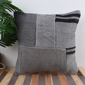 Può includere: Cuscino decorativo quadrato con un design patchwork in varie tonalità di grigio. Il cuscino presenta pannelli rettangolari di diverse trame e una sezione con strisce nere. Articolo per l'arredamento della casa.