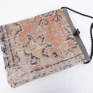 May include: A beige, blue, and orange patterned tote bag with a black adjustable strap and a wooden toggle closure.
