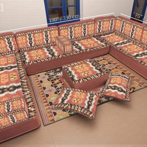 May include: A sectional sofa set with a patterned design in shades of red, orange, black, and cream. The set includes a large corner sofa, a rug, two ottomans, and two throw pillows. The sofa measures 130 inches by 75 inches, and the ottoman is 28 inches.