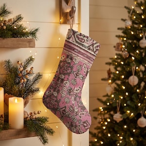 Op de afbeelding: Een kerstkous met een vintage tapijtpatroon in tinten roze, crème en donkergrijs. De kous heeft een omgeslagen boord aan de bovenkant en hangt aan een houten haak, met een gedetailleerd geweven textielontwerp.