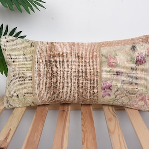 May include: A rectangular throw pillow with a patchwork design featuring beige, brown, and pink floral patterns. The pillow is made from a woven fabric and has a frayed edge.