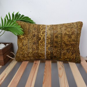 May include: A rectangular pillow with a gold and brown patterned fabric. The pillow is made from a vintage rug and has a white seam down the center.