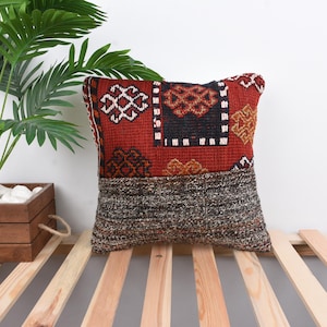 Pode incluir: Travesseiro de arremesso estampado em vermelho, preto e branco com um encosto de tecido tecido cinza e preto. O travesseiro está sobre uma superfície de ripas de madeira.