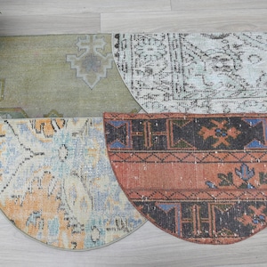 May include: Four half-circle vintage rugs in shades of green, beige, orange, and blue. Each rug features a unique distressed pattern, with visible wear and tear. The rugs are arranged on a light wood surface.