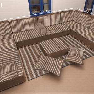 以下が含まれることがあります： 茶色と白のストライプ柄のコーナーソファセット。お揃いのラグ、2つのオットマン、2つのスローピローが含まれます。ソファの長さは330cm、幅は190cmです。ラグの幅は70cmです。「SET-1」の文字が見えます。