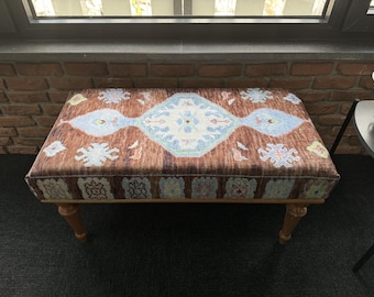 May include: A brown and blue patterned ottoman with wooden legs. The ottoman has a traditional design with intricate details.