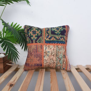 May include: A square throw pillow with a patchwork design featuring various shades of blue, green, orange, and brown. The pillow is made from a woven fabric with a vintage look.