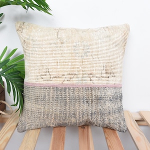Puede incluir: Una almohada decorativa con un patrón tejido beige y gris. La almohada tiene una franja rosa en el medio.