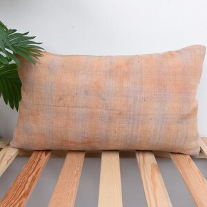 May include: A rectangular, light orange throw pillow with a woven texture. The pillow is lying on a wooden slatted surface.