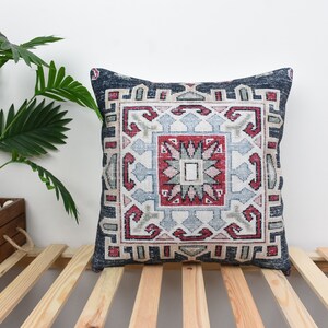 May include: A decorative throw pillow with a blue, red, and white geometric pattern. The pillow is on a wooden slatted surface.