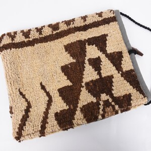 May include: A beige and brown woven bag with a geometric pattern. The bag has a black drawstring closure and a black shoulder strap.