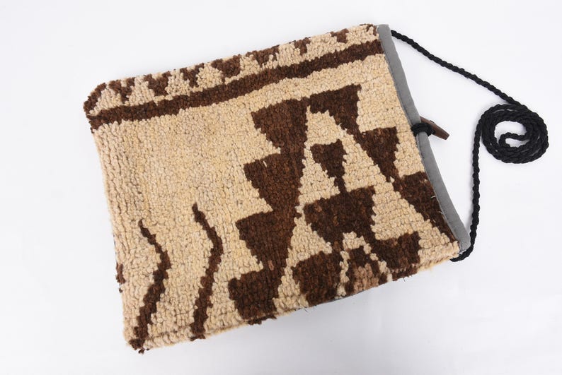 May include: A beige and brown woven bag with a geometric pattern. The bag has a black drawstring closure and a black shoulder strap.